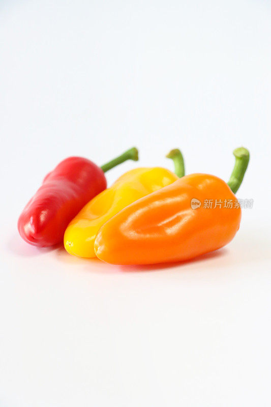 图像对角线排列的三个，交替红、黄、橙迷你辣椒(Capsicum annuum)，白色背景，重点放在前景，复制空间